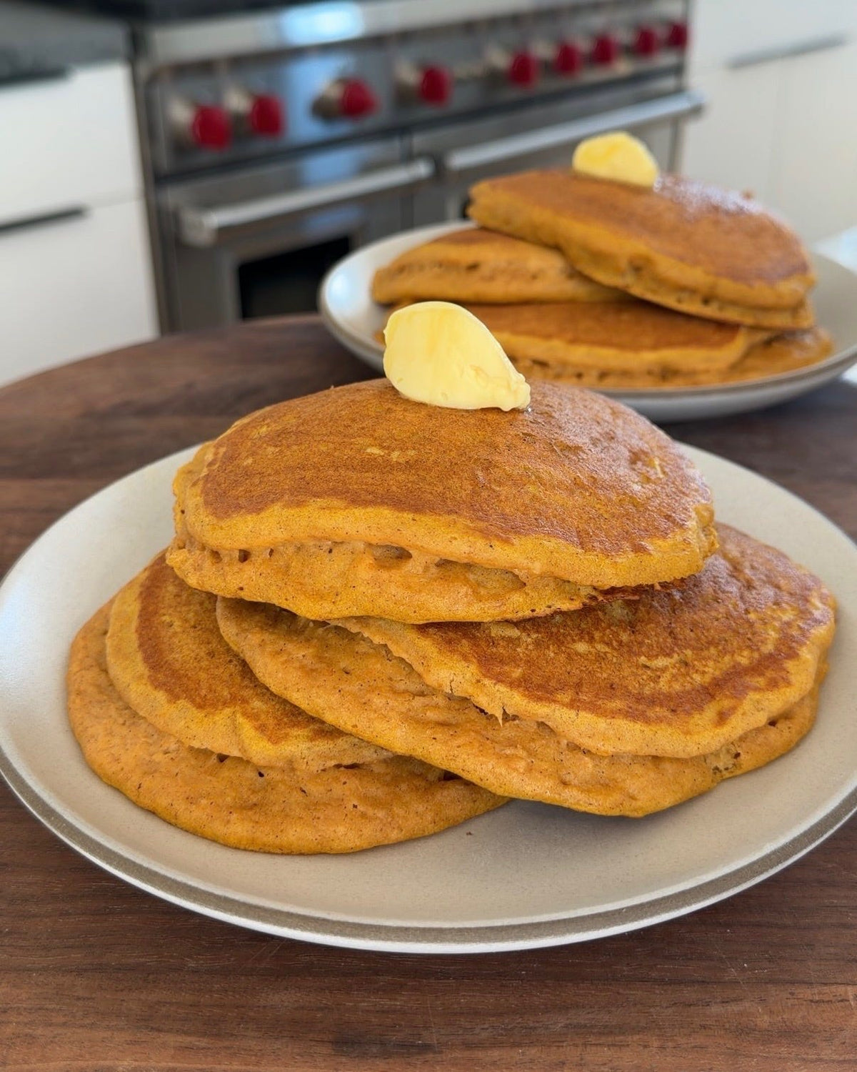 Two stacks of golden pumpkin spice pancakes topped with melting creamed honey