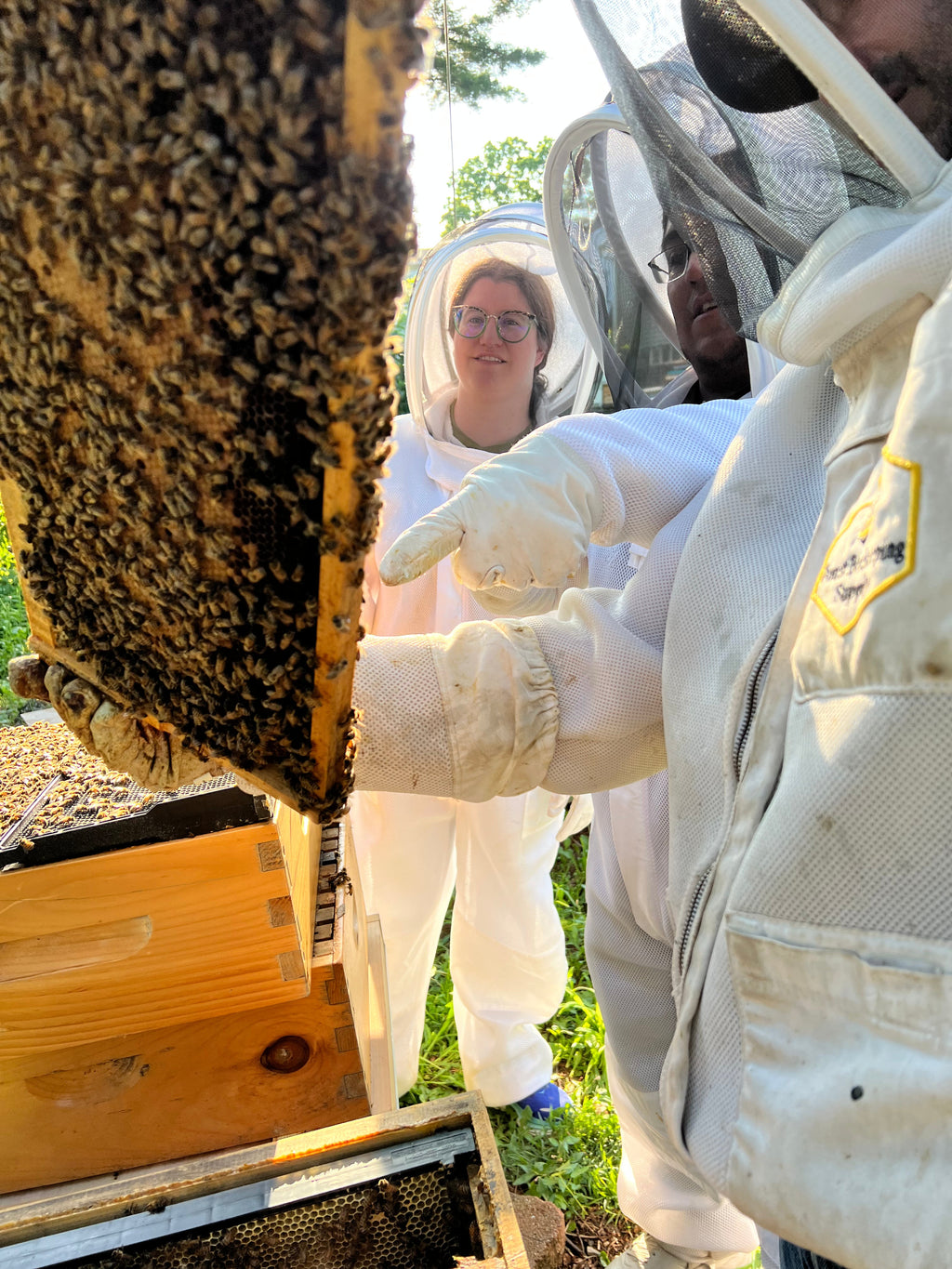 Two people wearing white protective beekeeping suits and gloves during a Barley Moon Botanicals hive adventure date.