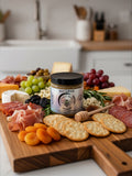 Barley Moon Botanicals Aji Limo Creamed Honey jar centered on a gourmet charcuterie board with meats, cheese, and fruit.