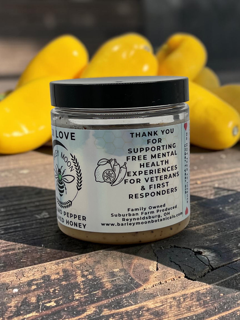 Barley Moon Botanicals Aji Limo creamed honey jar with a black lid, displayed in front of fresh yellow Aji Limo peppers.