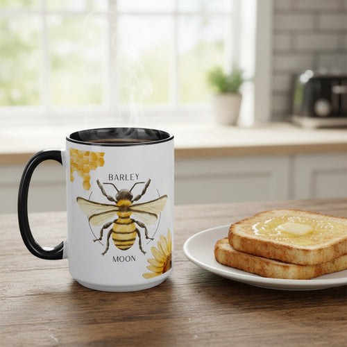 Barley Moon Botanicals 15oz ceramic mug with bee and flower design, black handle and interior, on a wooden table.