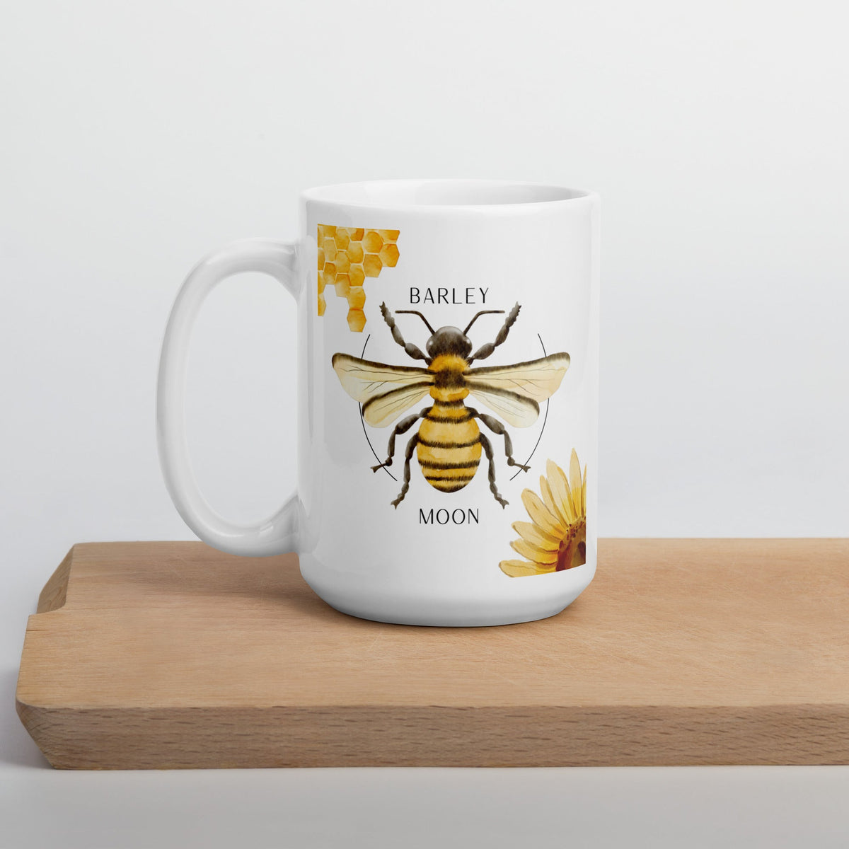 Barley Moon Botanicals 15 oz white ceramic mug featuring a bee, honeycomb, and flower illustration on a wooden board.