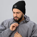 Bearded man wearing a black Barley Moon Botanicals cuffed beanie with a white bee and moon logo on a grey background