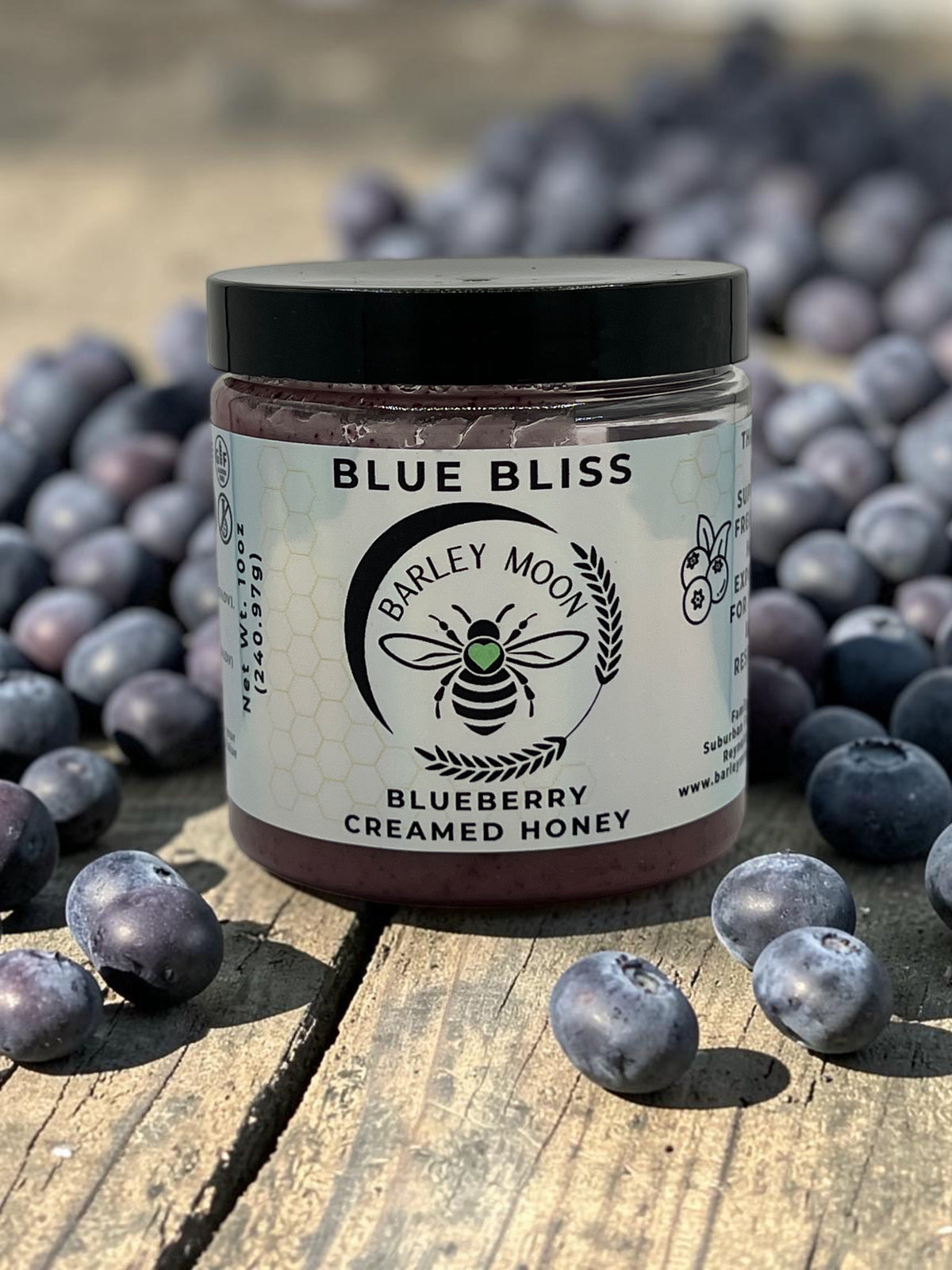 Barley Moon Botanicals Blue Bliss blueberry creamed honey jar surrounded by fresh blueberries on a rustic wood surface