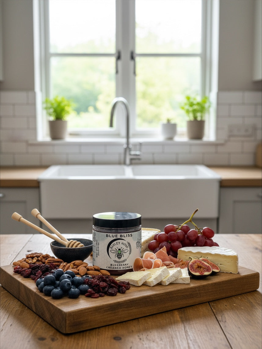Barley Moon Botanicals Blue Bliss blueberry creamed honey jar on a charcuterie board with fruit, nuts, and cheese.