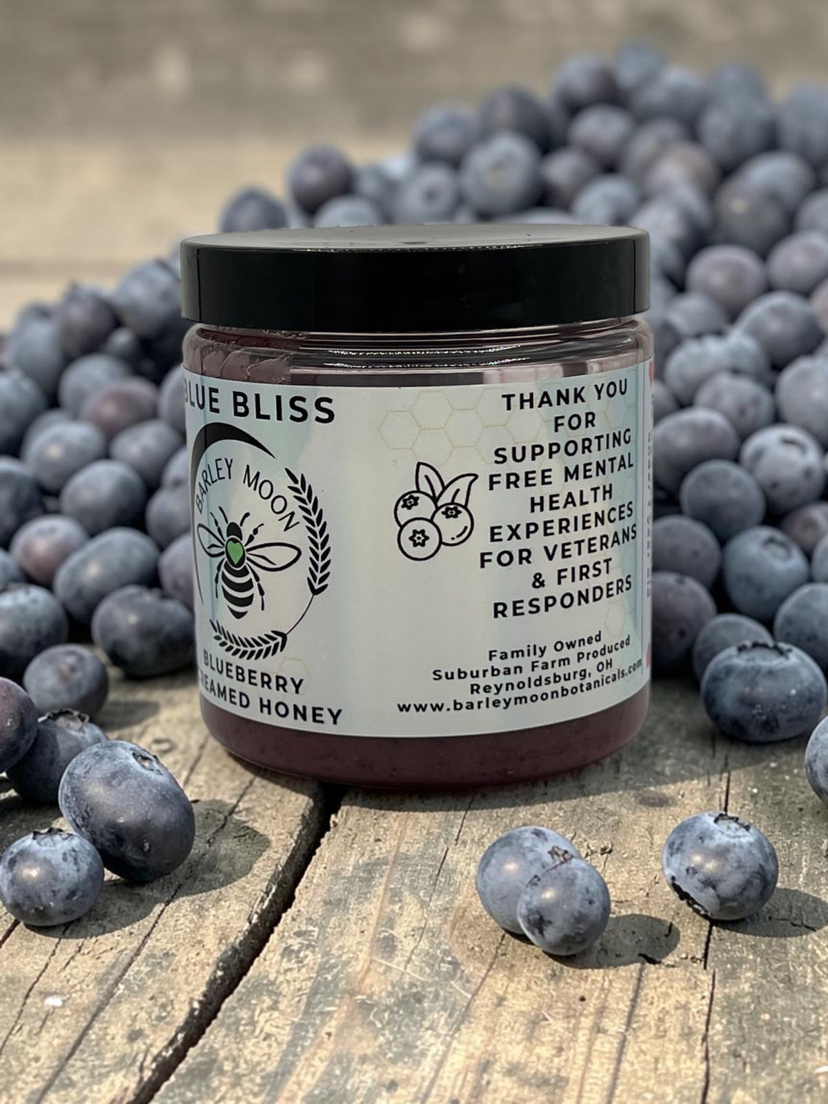 Barley Moon Botanicals Blue Bliss blueberry creamed honey jar surrounded by fresh blueberries on a wooden surface