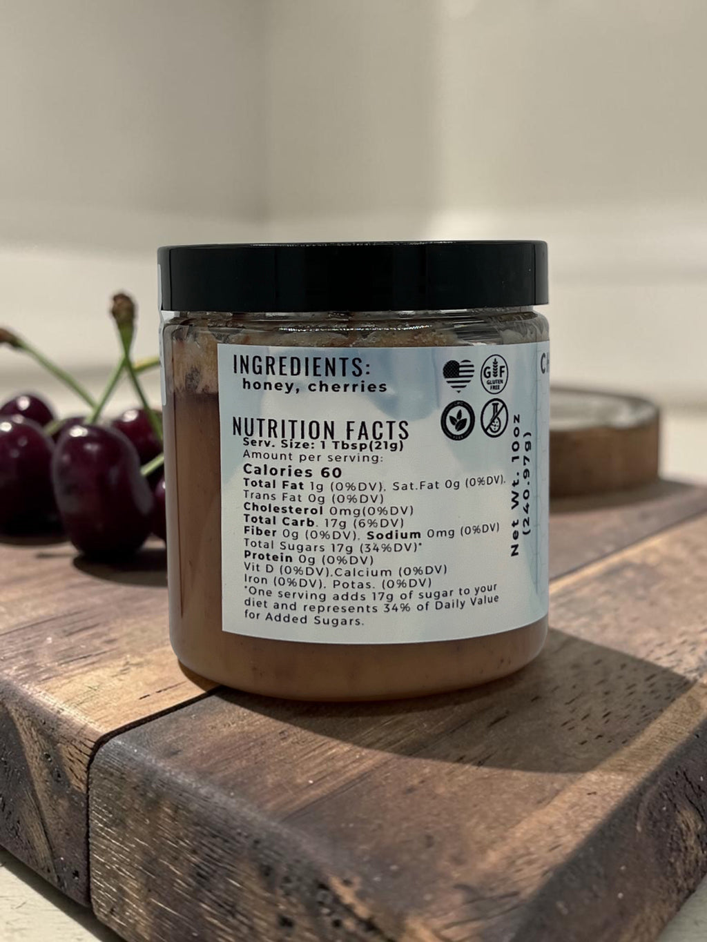 Barley Moon Botanicals Cheery Cherry creamed honey jar showing nutrition facts label with fresh cherries on wood board