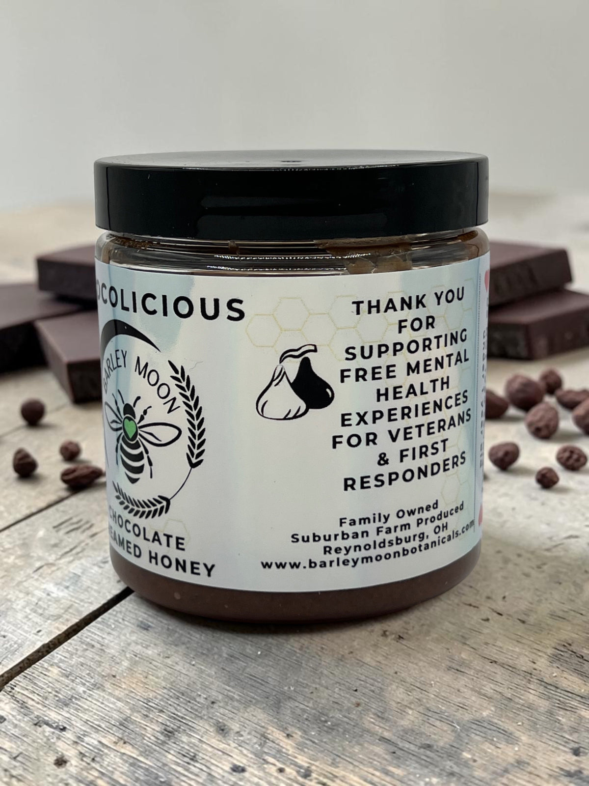 Barley Moon Botanicals Chocolicious chocolate creamed honey jar on a rustic wooden surface with dark chocolate pieces.
