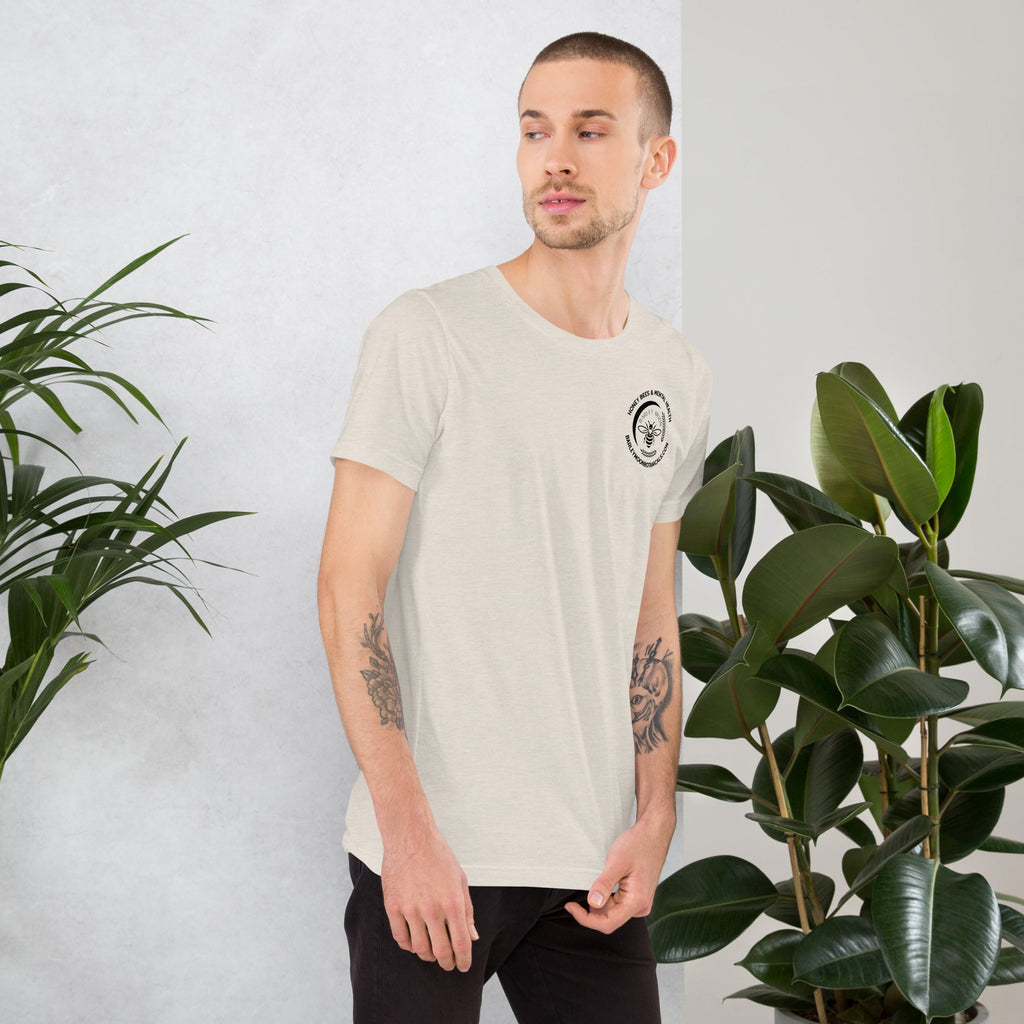 A man wearing a Barley Moon Botanicals unisex cream t-shirt with a small bee logo on the chest, standing by plants.