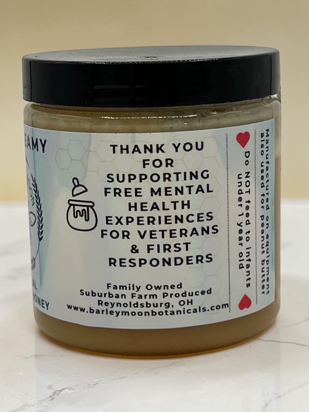 Barley Moon Botanicals Just Creamy original creamed honey jar with mission statement label on a white surface