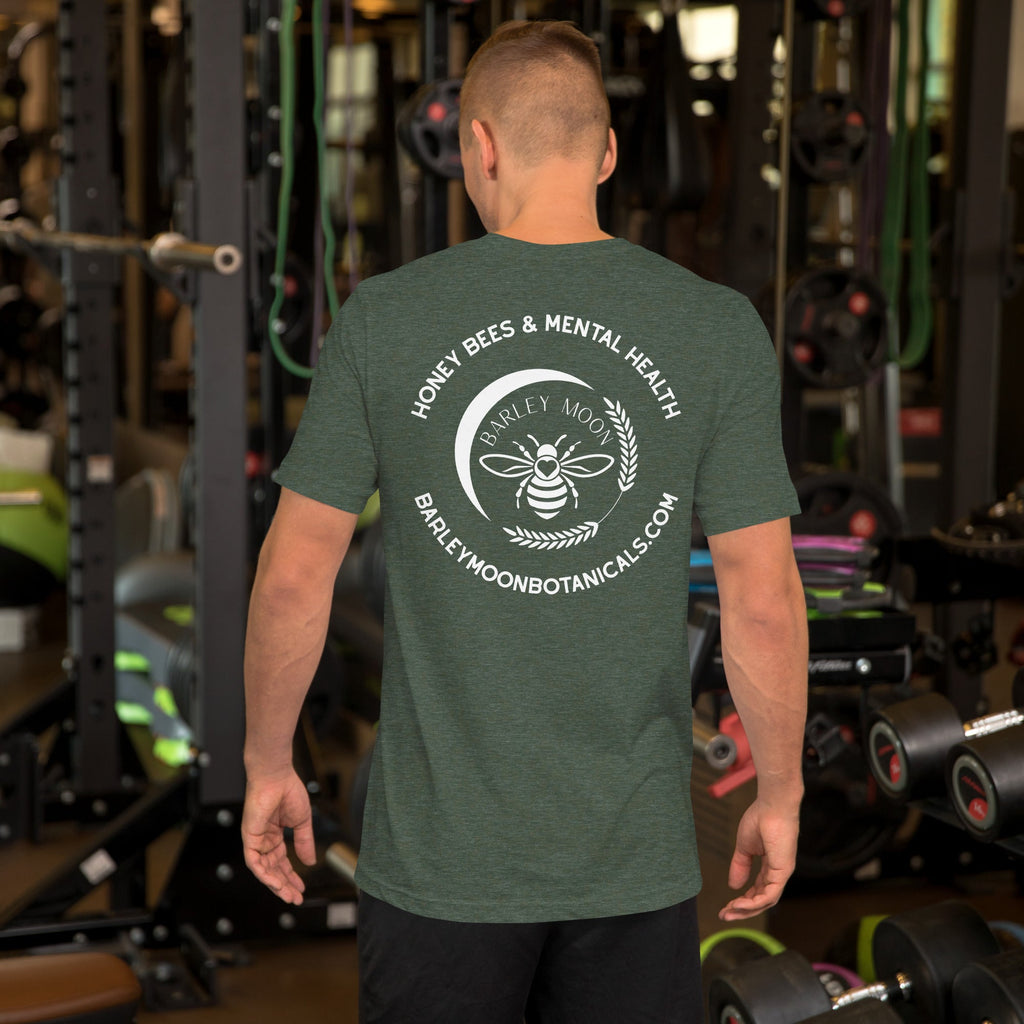 Man wearing a green Barley Moon Botanicals t-shirt with a white bee and crescent moon logo in a gym setting.