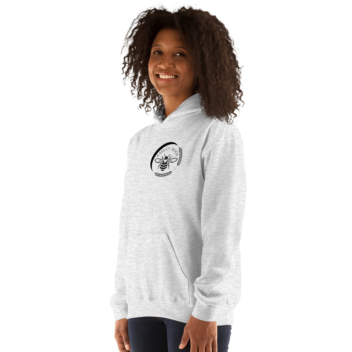 A woman wearing a Barley Moon Botanicals light grey unisex hoodie with a black bee and crescent moon logo on the chest