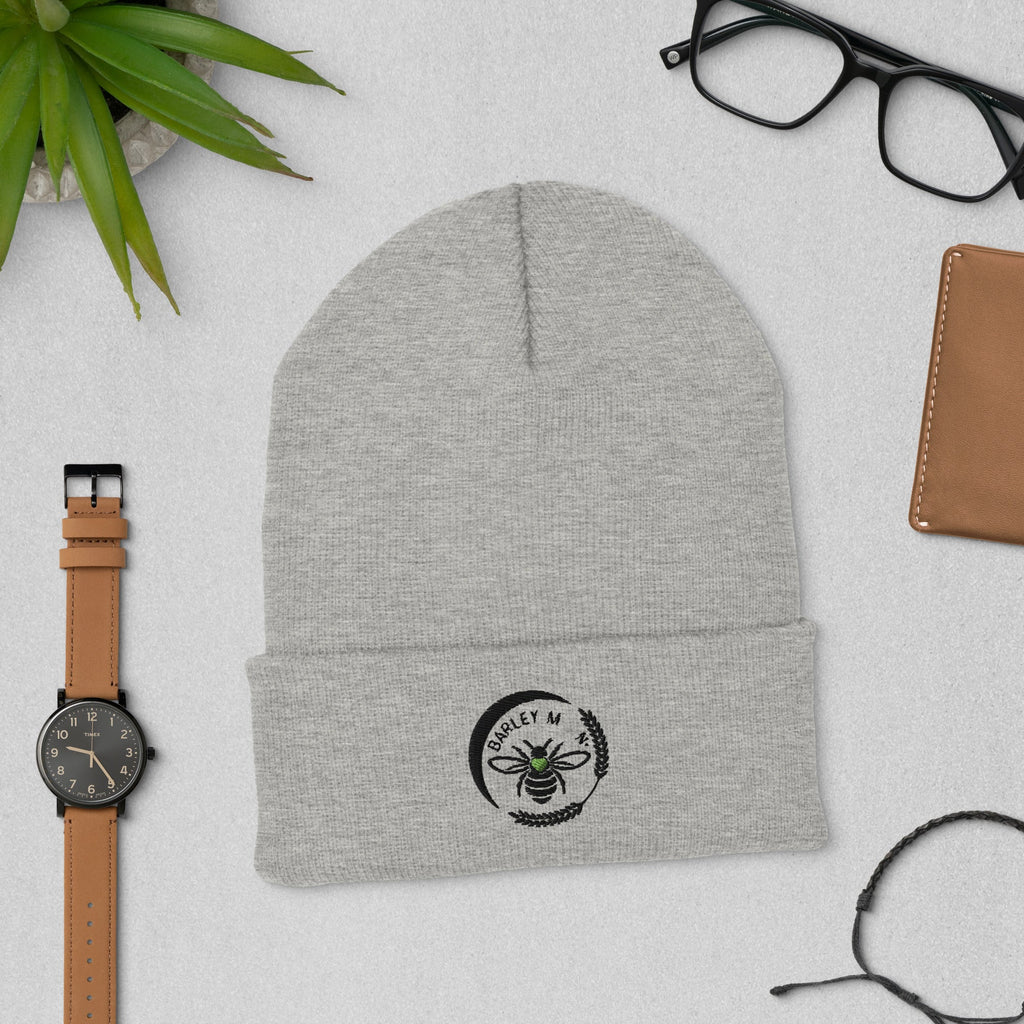 Barley Moon Botanicals grey cuffed beanie with a black bee and moon logo, displayed on a flat lay desk surface.