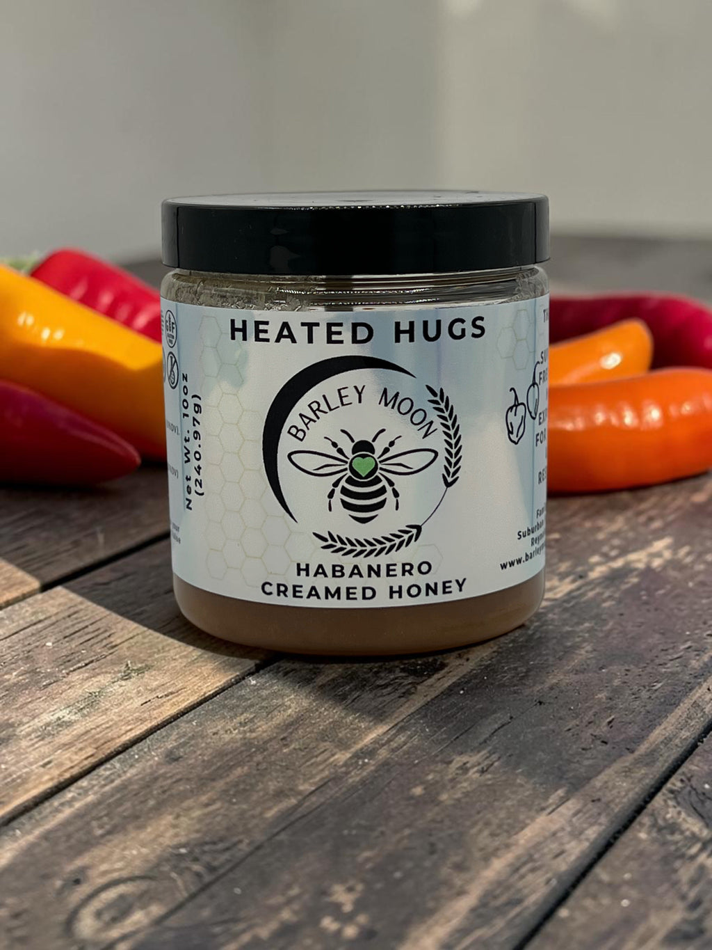 Barley Moon Botanicals Heated Hugs habanero creamed honey in a glass jar with fresh chili peppers on a wooden table.