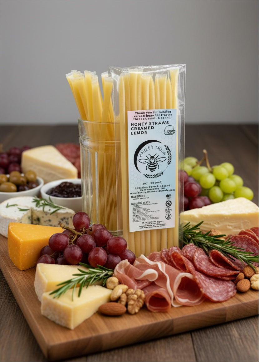 Barley Moon Botanicals lemon creamed honey straws in a glass jar on a charcuterie board with cheese, meat, and fruit.