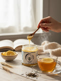 Barley Moon Botanicals Lovely Lemon creamed honey being scooped with a wooden spoon near tea and fresh lemon slices.