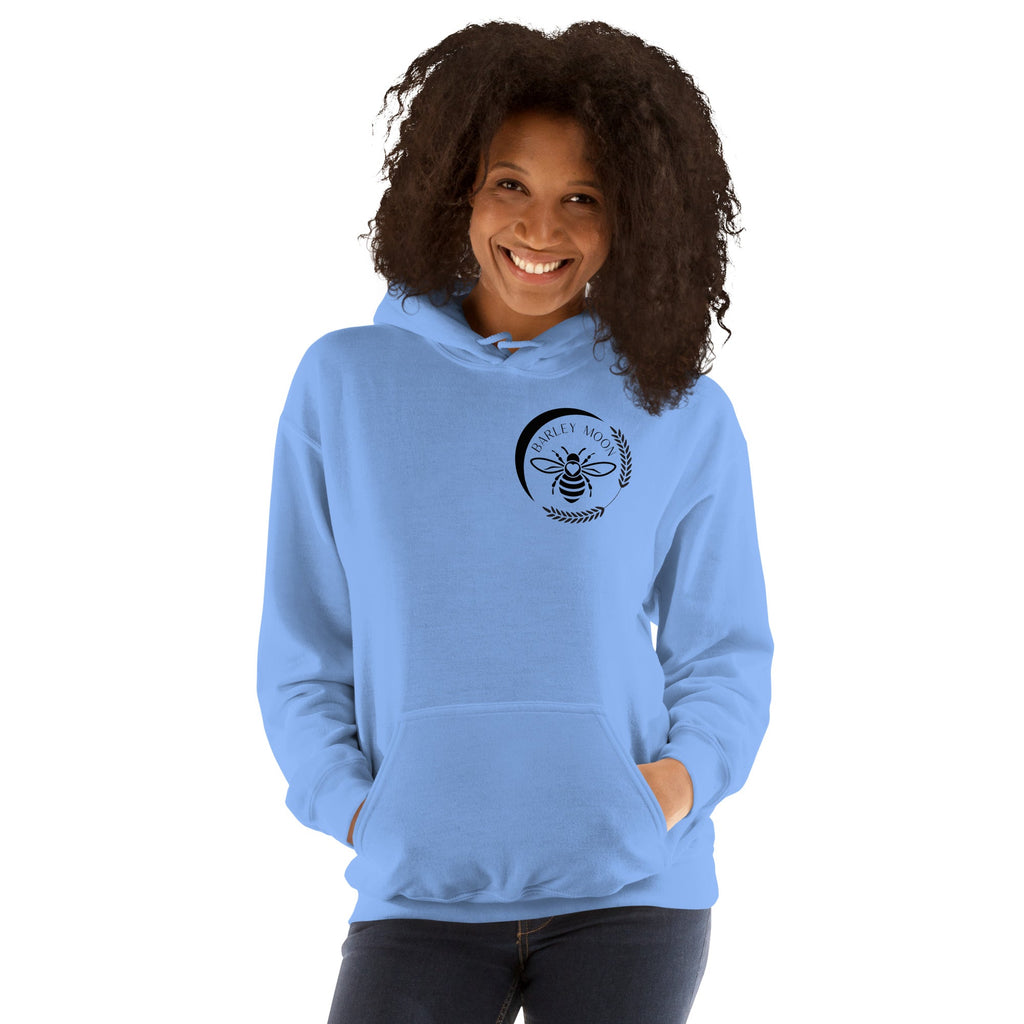 Woman wearing a light blue Barley Moon Botanicals unisex hoodie with a black bee and crescent moon chest logo