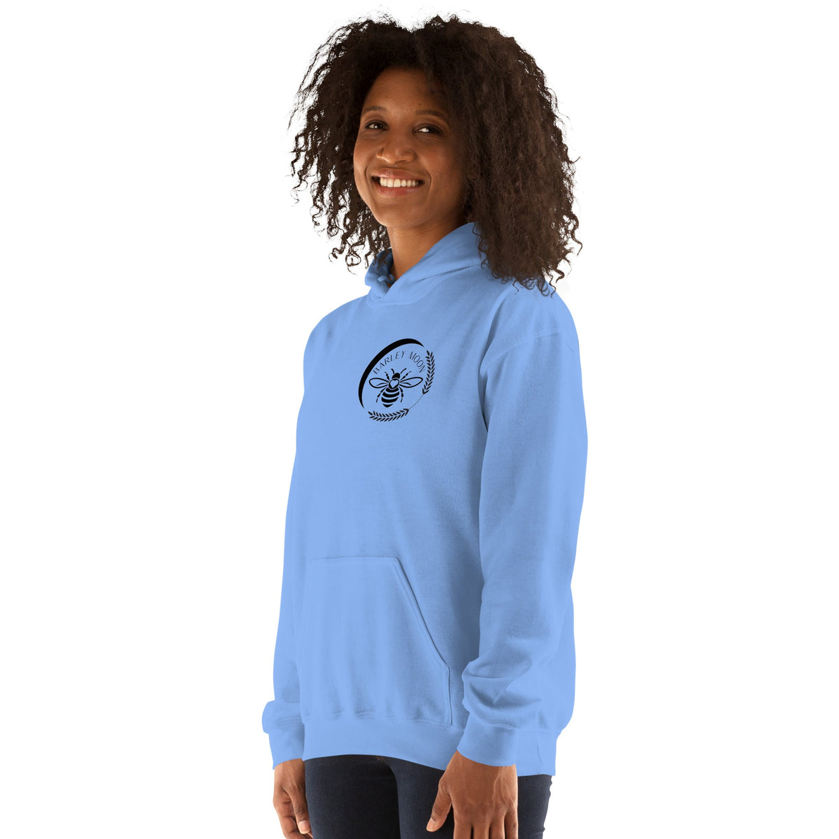 A woman wearing a light blue Barley Moon Botanicals unisex hoodie with a black bee and crescent moon logo on the chest.