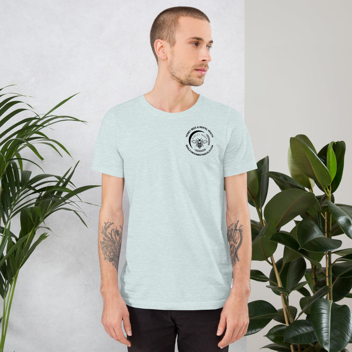 A man wearing a light blue Barley Moon Botanicals unisex t-shirt with a small black bee logo on the chest.