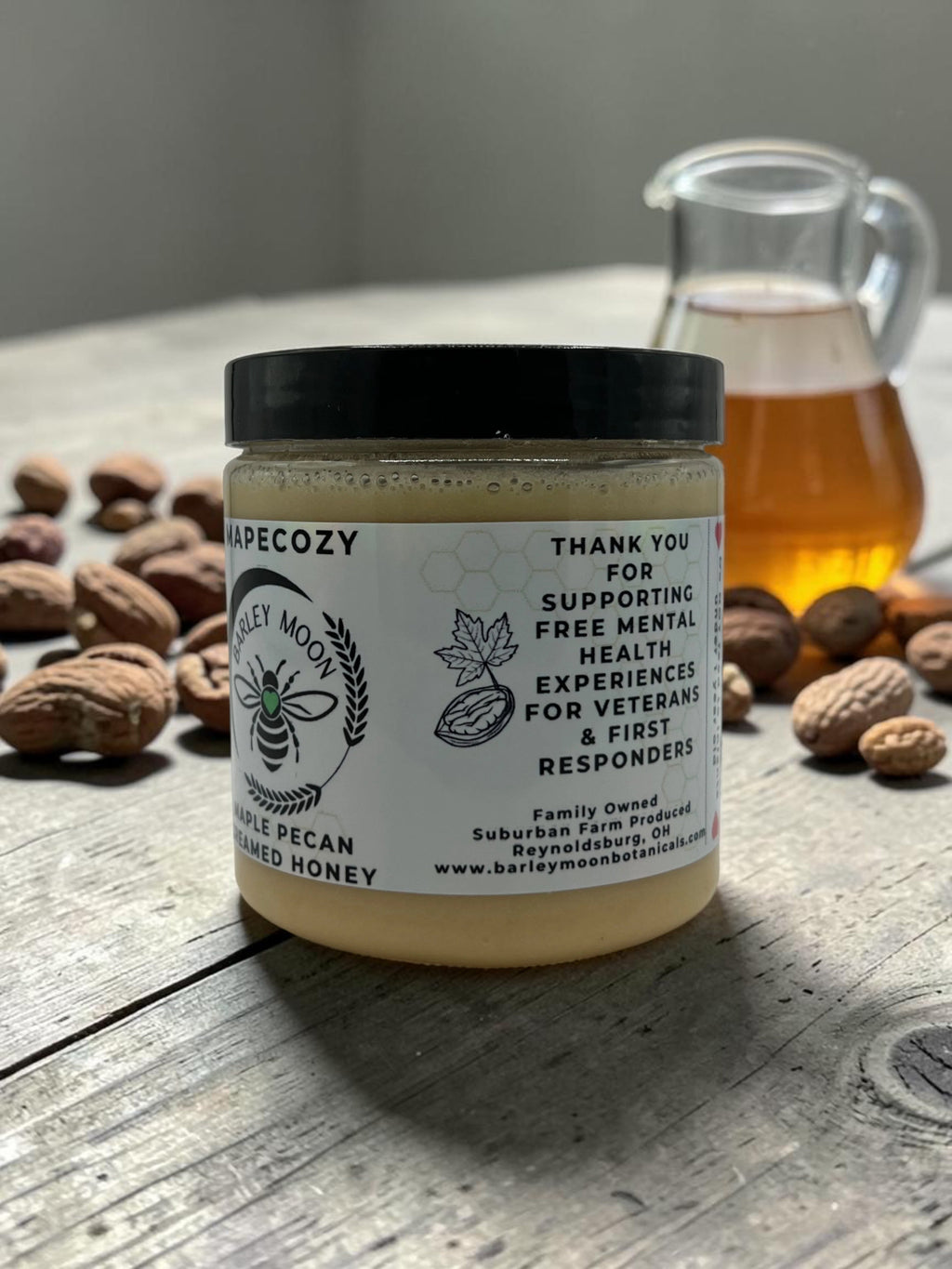 Barley Moon Botanicals MapeCozy maple pecan creamed honey jar on a rustic wooden table with pecans and honey syrup.