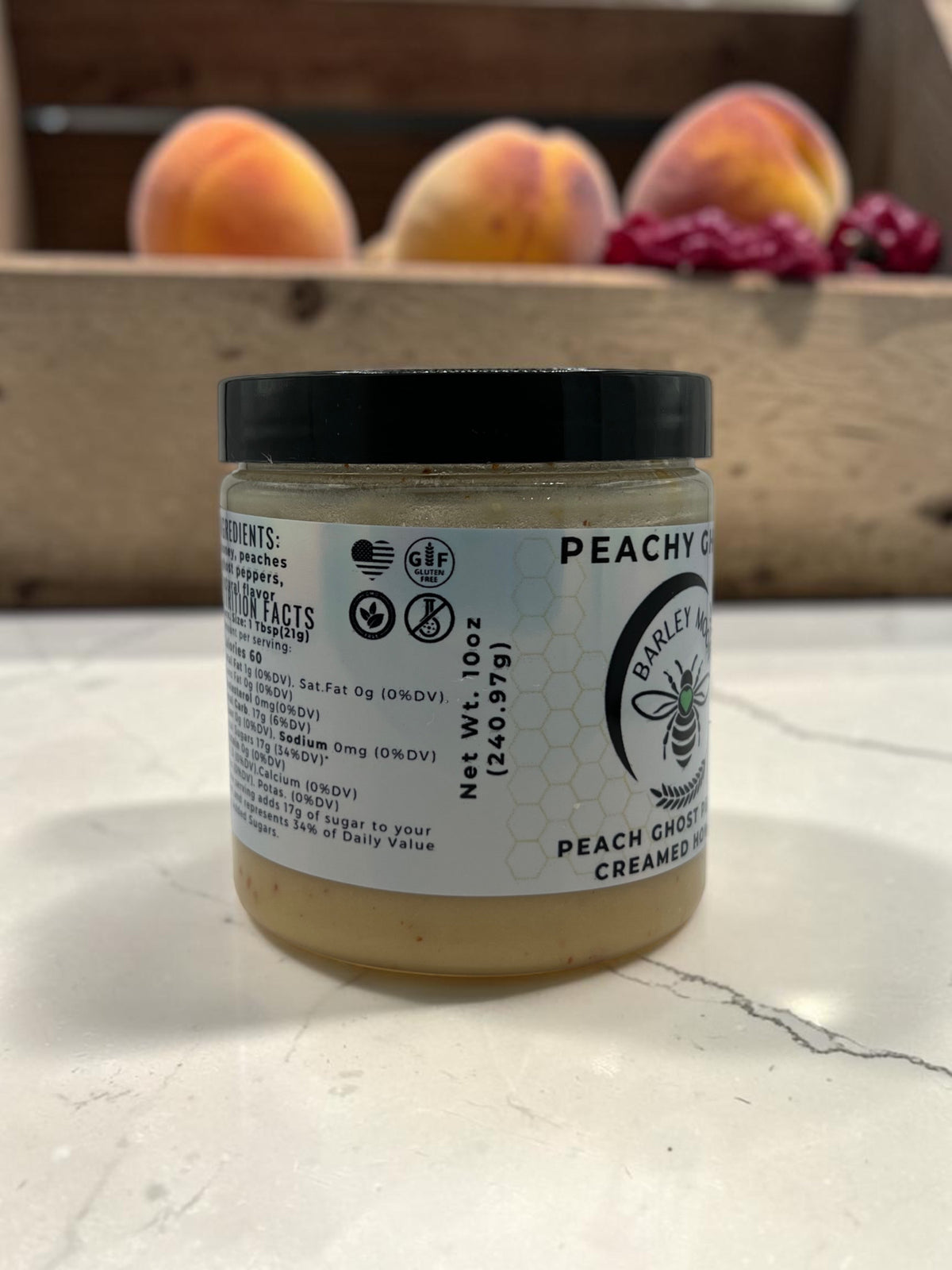Barley Moon Botanicals Peachy Ghost creamed honey jar with peach and ghost peppers on a white marble surface