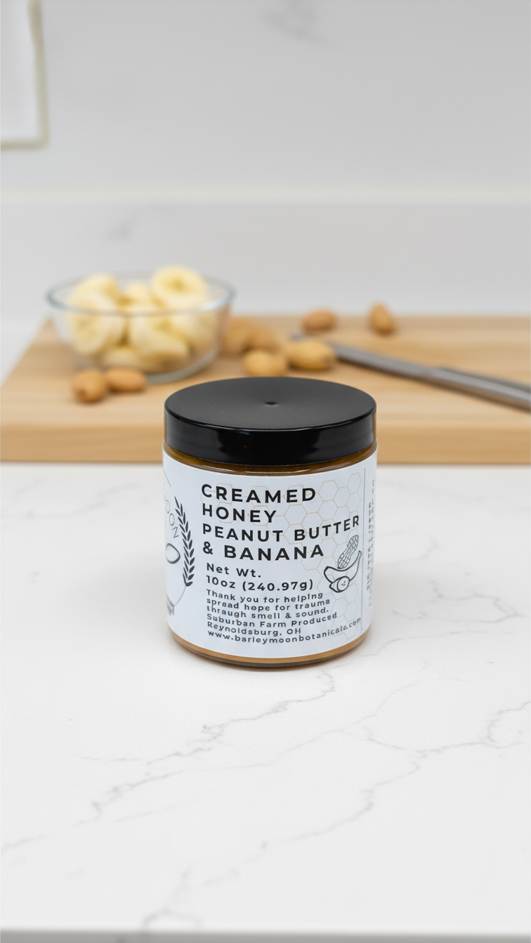 Barley Moon Botanicals Nutty Nana peanut butter and banana creamed honey jar on a kitchen counter with fresh fruit