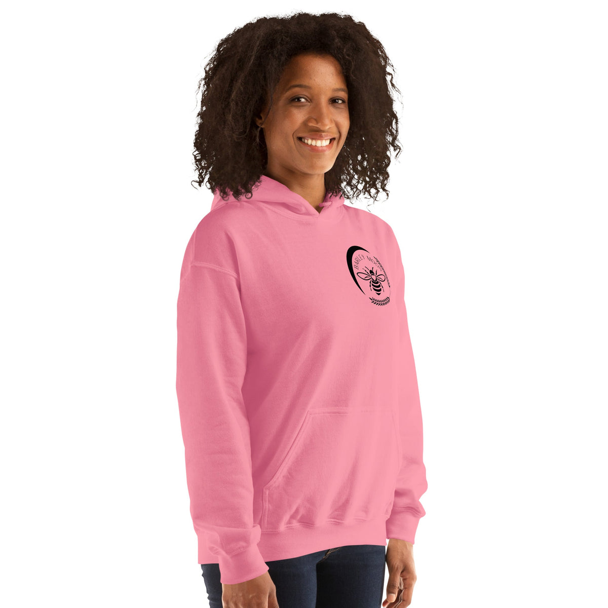 A woman wearing a pink Barley Moon Botanicals unisex hoodie featuring a black bee and crescent moon logo on the chest.