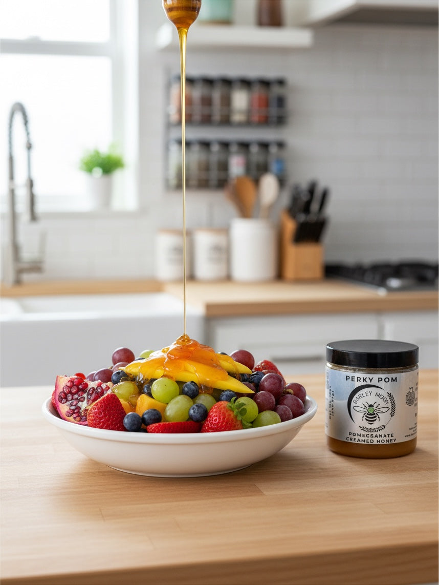 Barley Moon Botanicals Perky Pom pomegranate creamed honey drizzled over a fresh fruit bowl on a kitchen counter