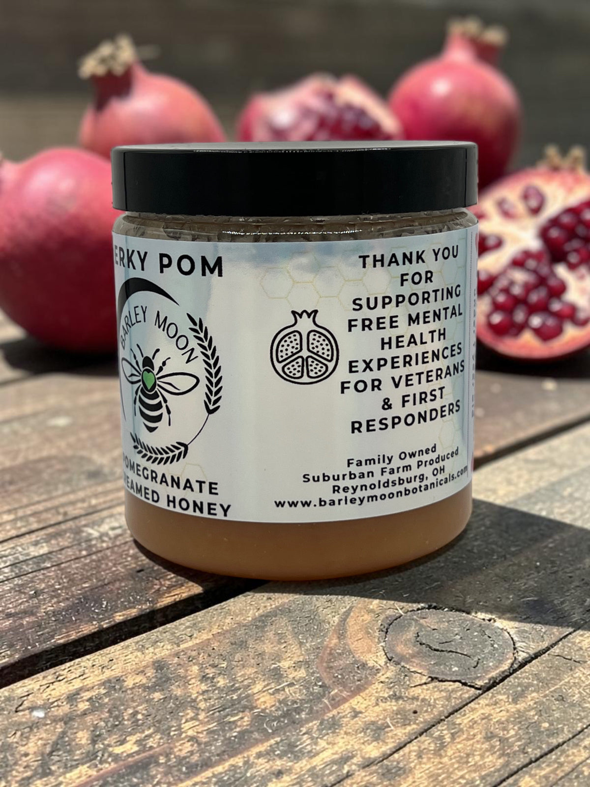 Barley Moon Botanicals Perky Pom pomegranate creamed honey jar on a wooden surface with fresh pomegranates behind
