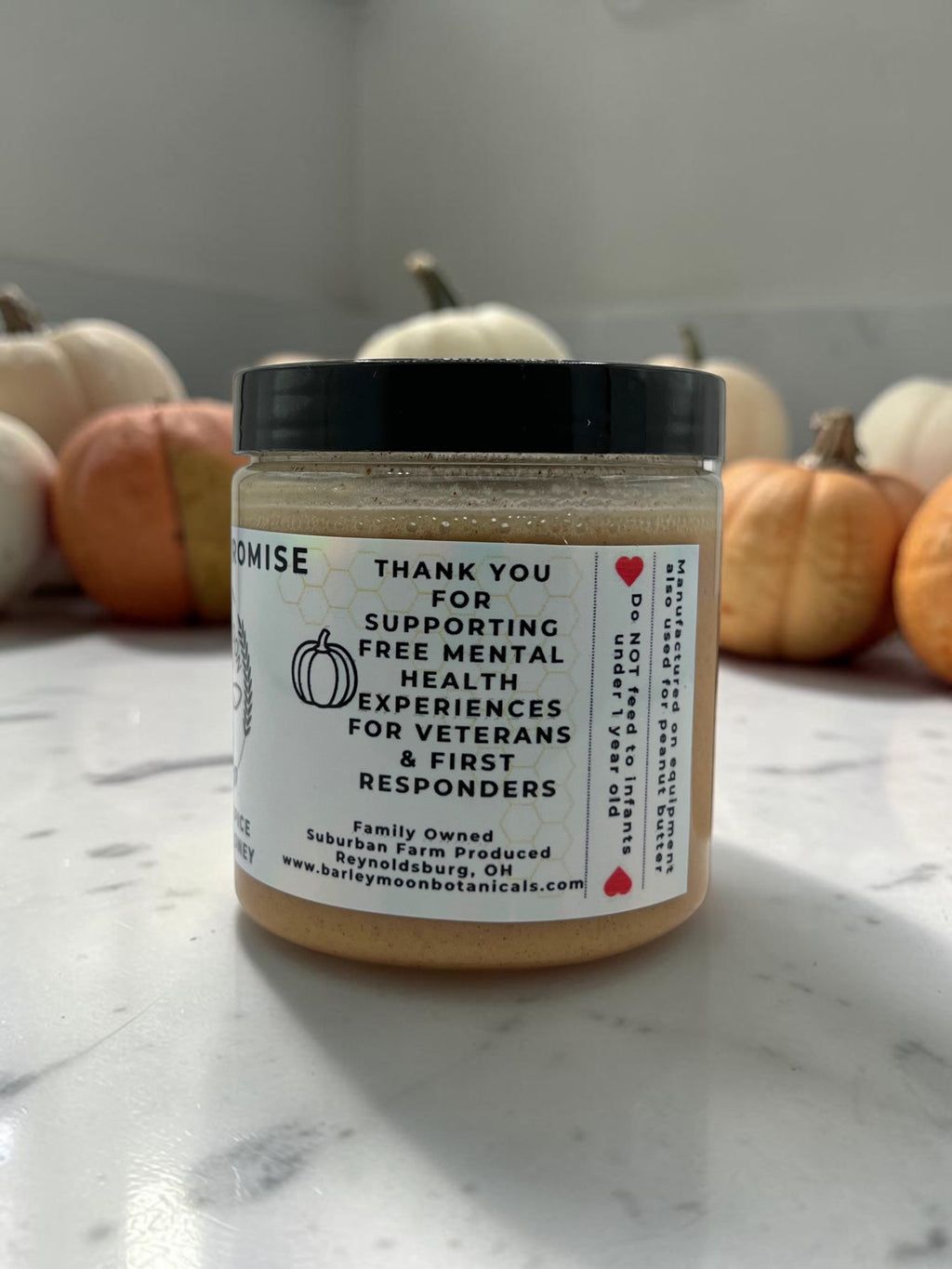 Barley Moon Botanicals Pumpkin Promise creamed honey jar with spice blend label, set against small decorative pumpkins.