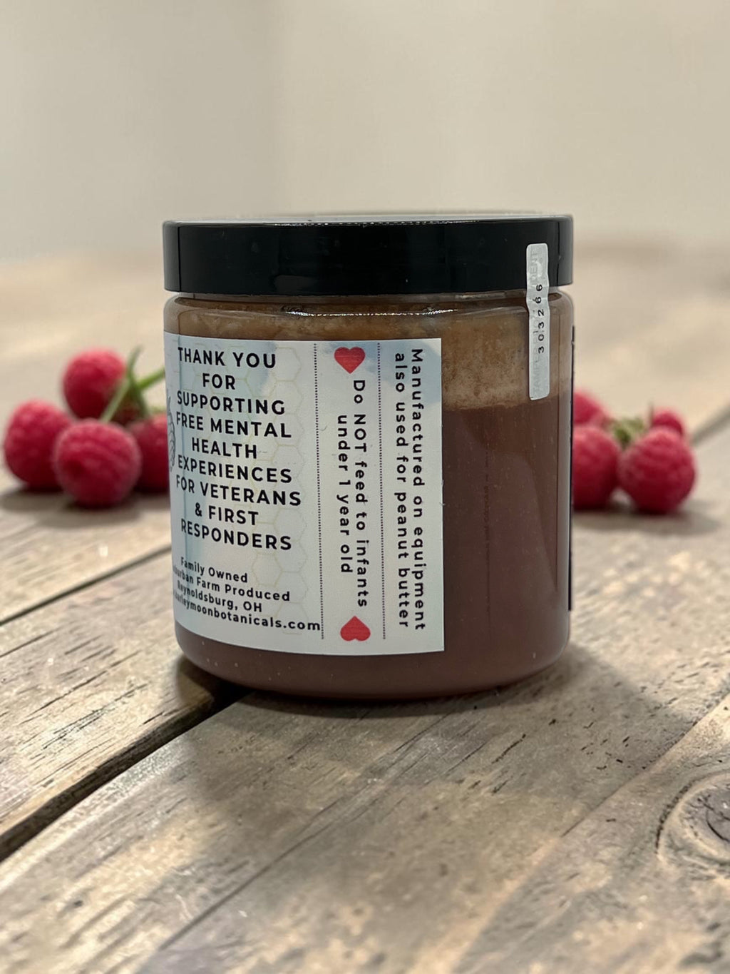 Barley Moon Botanicals Regal Razzle raspberry creamed honey in a glass jar on a wooden table with fresh raspberries.