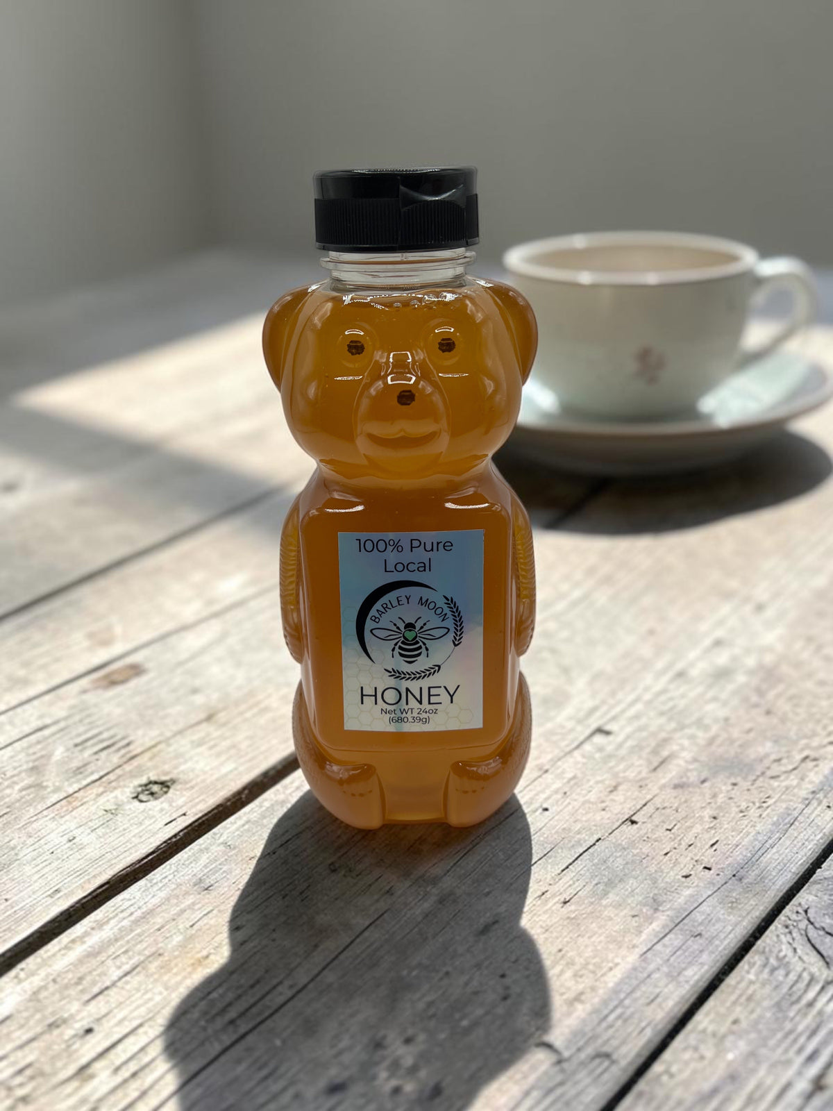Barley Moon Botanicals raw local honey in a 24 oz bear-shaped bottle sitting on a rustic wooden table.