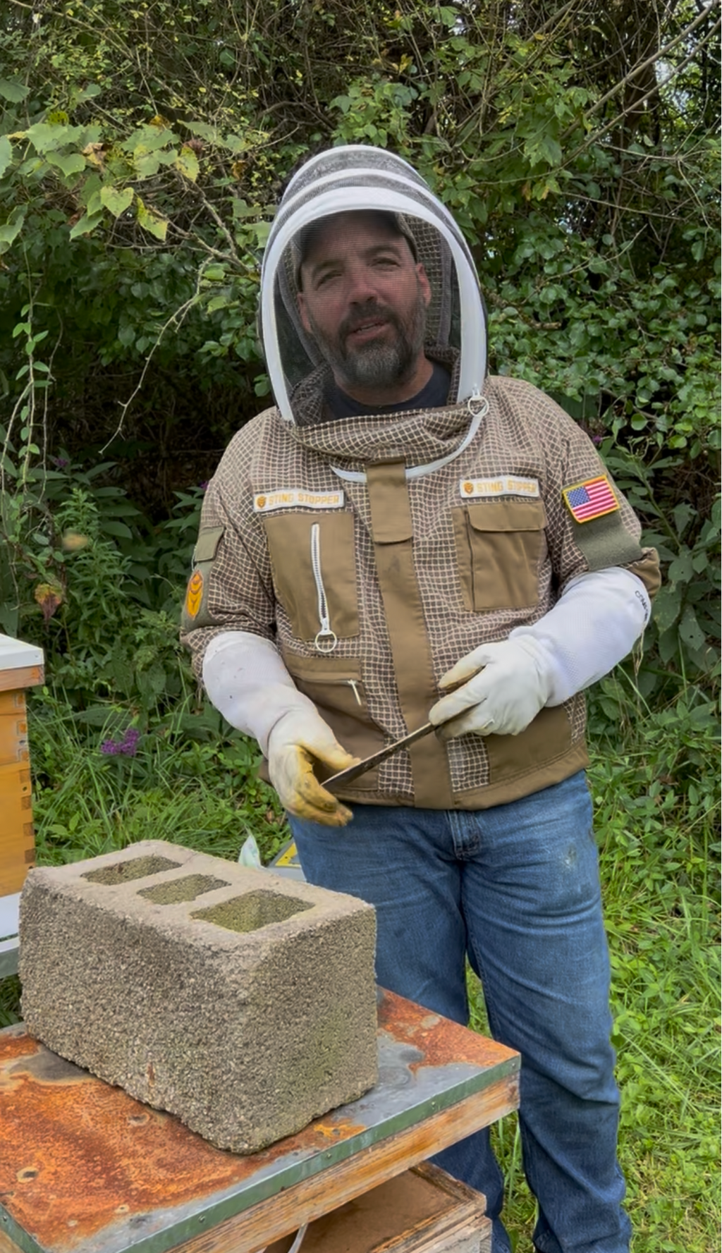 Beekeeper in protective gear leading a Barley Moon Botanicals therapeutic hive experience in a lush outdoor setting.