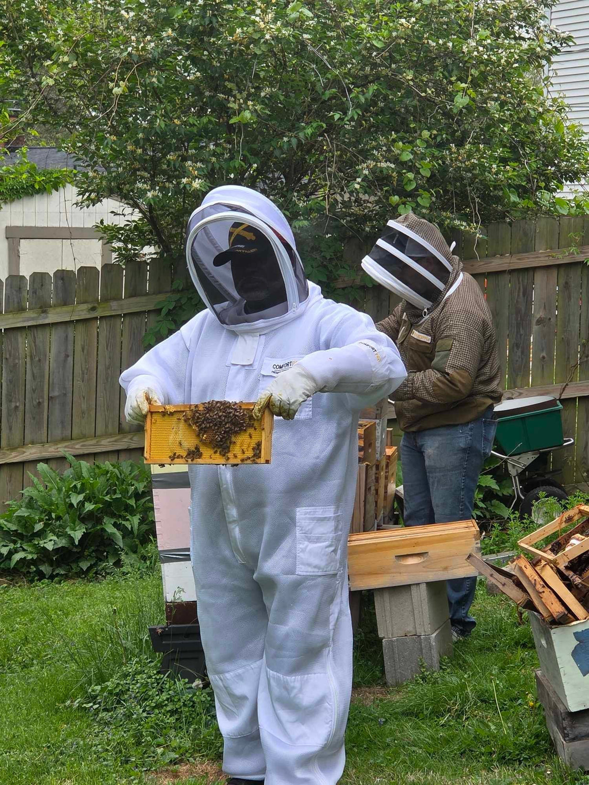 Barley Moon Botanicals therapeutic hive experience with a beekeeper in a white protective suit holding a bee frame.