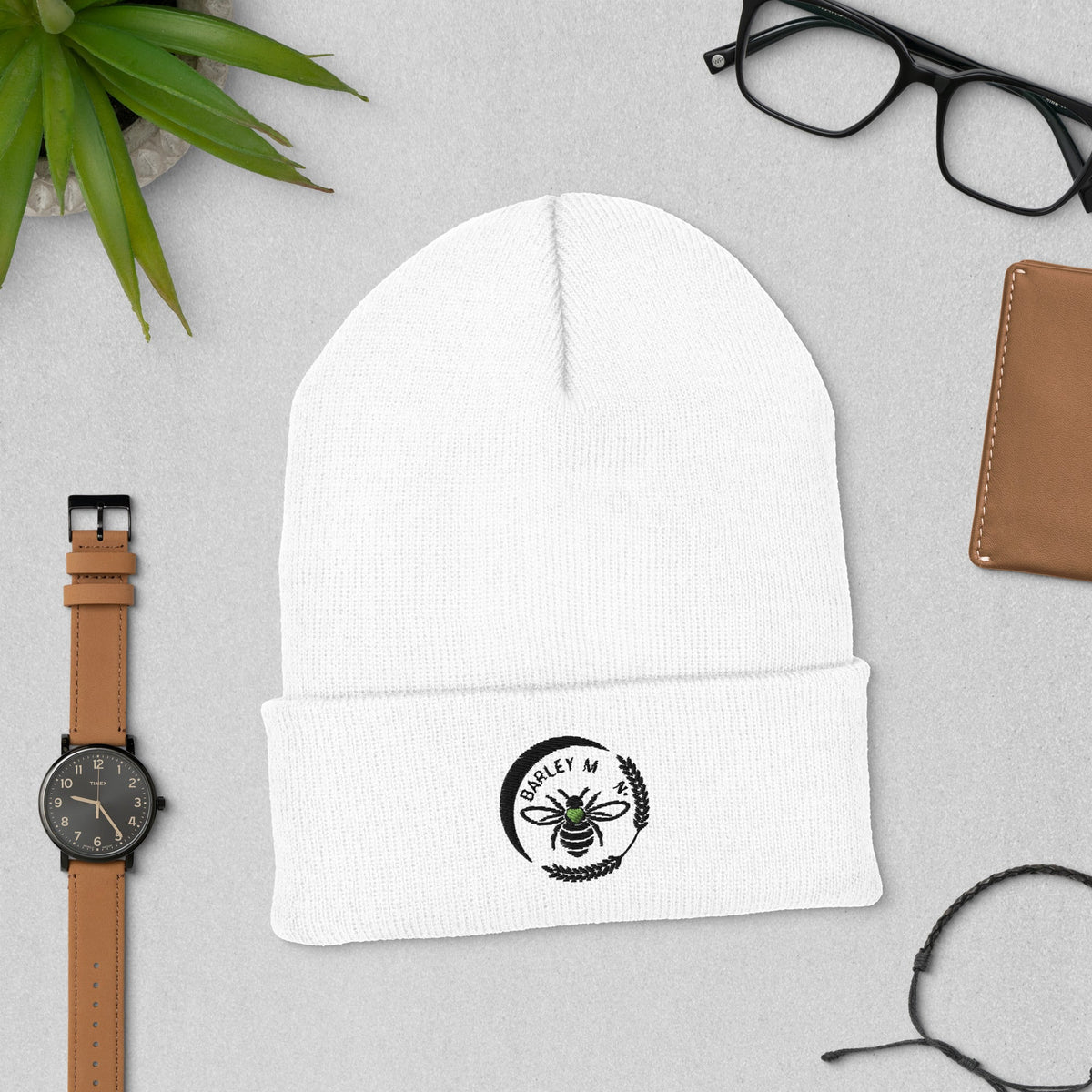 Barley Moon Botanicals white cuffed beanie with black bee and moon logo embroidery on a grey desk background