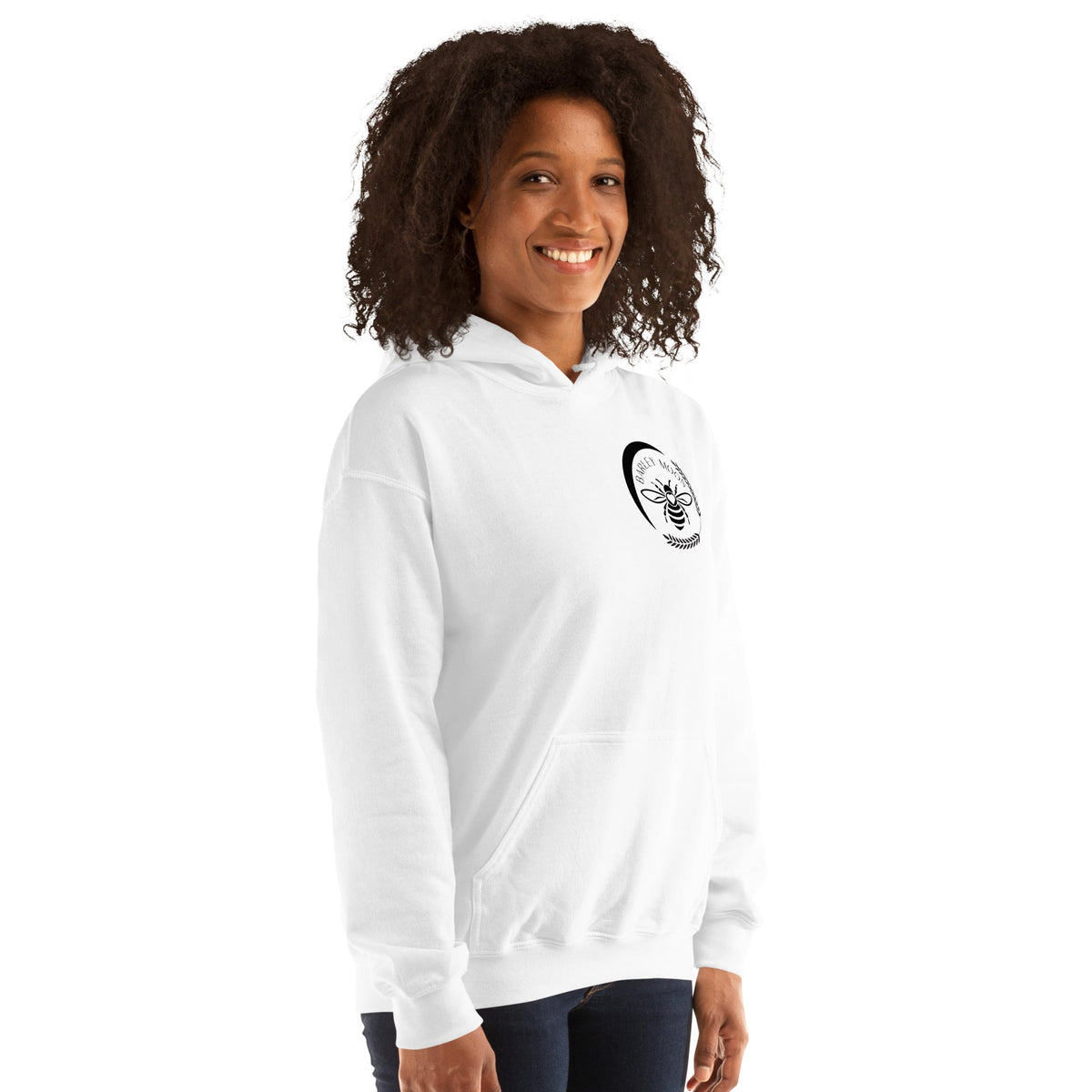 A woman wearing a white Barley Moon Botanicals unisex hoodie featuring a black bee and crescent moon logo on the chest.