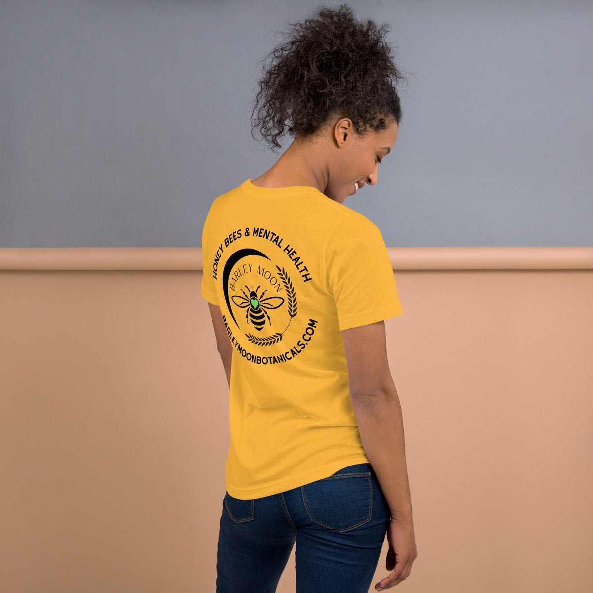 Woman wearing a yellow Barley Moon Botanicals t-shirt with a black bee and crescent moon logo on the back